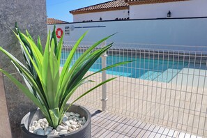 A pool area with a tiled deck, a metal fence, and a potted plant with green leaves.