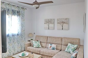 A living room with a beige sofa, floral cushions, a ceiling fan, and two wall-mounted paintings of trees. - Fabulous holiday home with private pool (Conil de la Frontera)