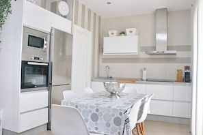 A modern kitchen with white cabinetry, a built-in oven, a microwave, a stainless steel sink, and a dining table with a patterned tablecloth. - Fabulous holiday home with private pool (Conil de la Frontera)