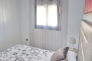 A bedroom with a bed, a window with sheer curtains, a bedside lamp, and a floral-patterned bedspread.