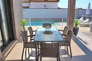 An outdoor patio with a glass table and wicker chairs, overlooking a swimming pool.