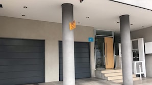 Entrada de un edificio moderno con camino de acceso cubierto, una rampa accesible para sillas de ruedas y un letrero que indica zona de carga.