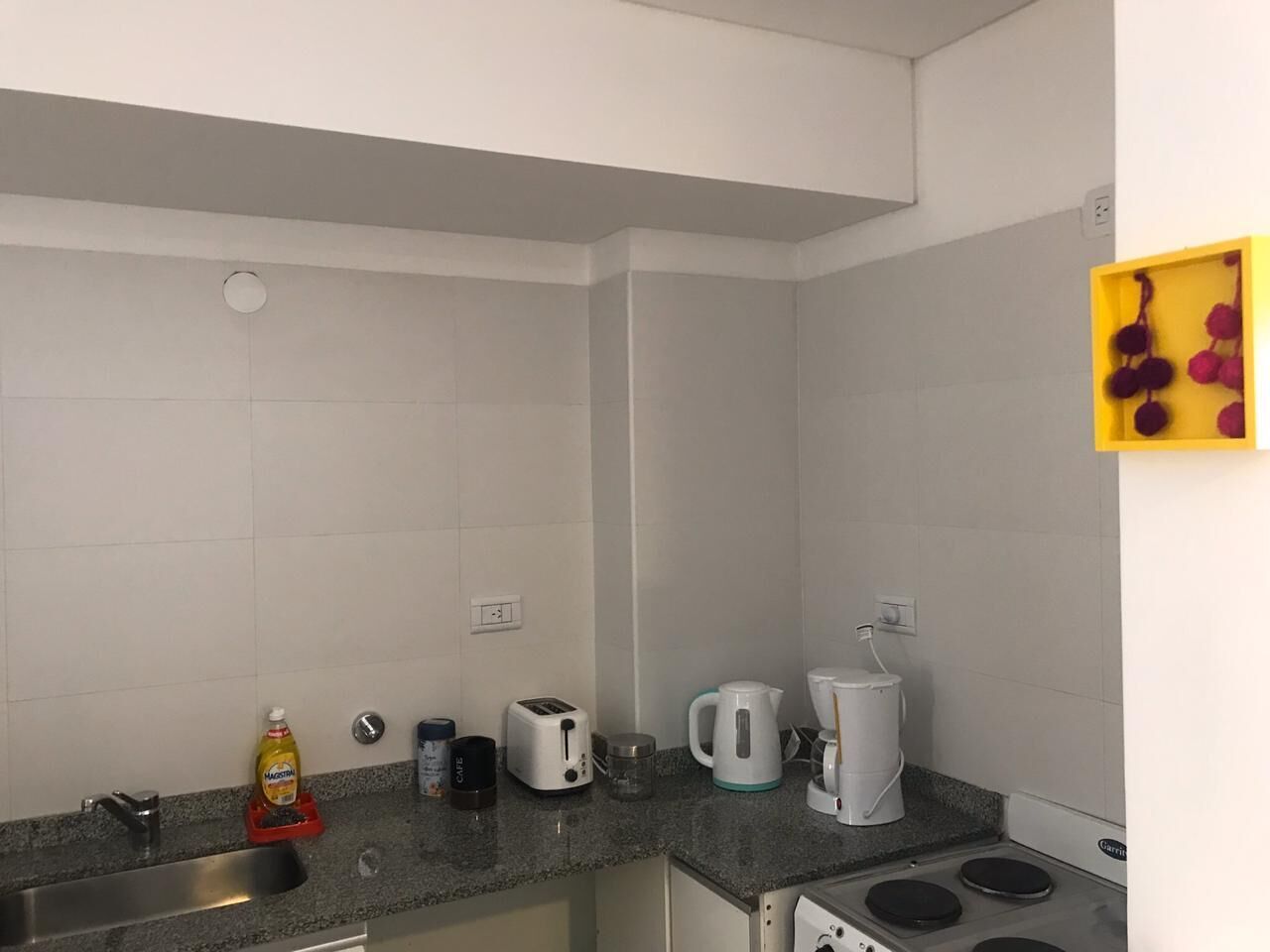 A compact kitchen with a sink, a toaster, a kettle, and a coffee maker.