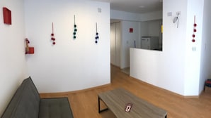 Una sala de estar moderna con un sofá, una mesa de centro de madera y una cocina visible a través de un arco abierto.