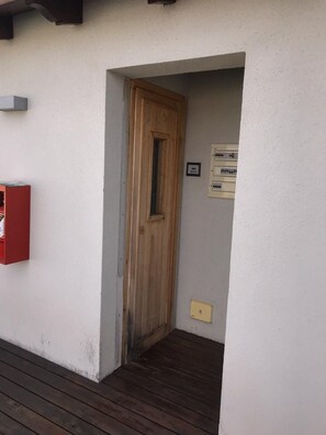 A wooden door leading to a room with a white wall and a small electrical panel.