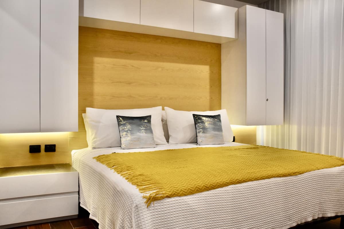 A modern bedroom with a wooden headboard, white bedding, and a mustard-colored throw blanket.