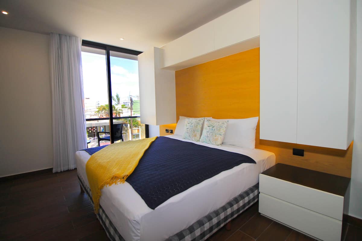 A modern hotel room with a large bed, a nightstand, a wardrobe, and a balcony with a view.