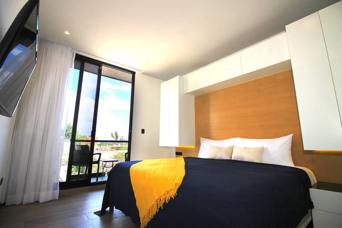 A modern hotel room with a large bed, a wooden headboard, and a balcony with a view.