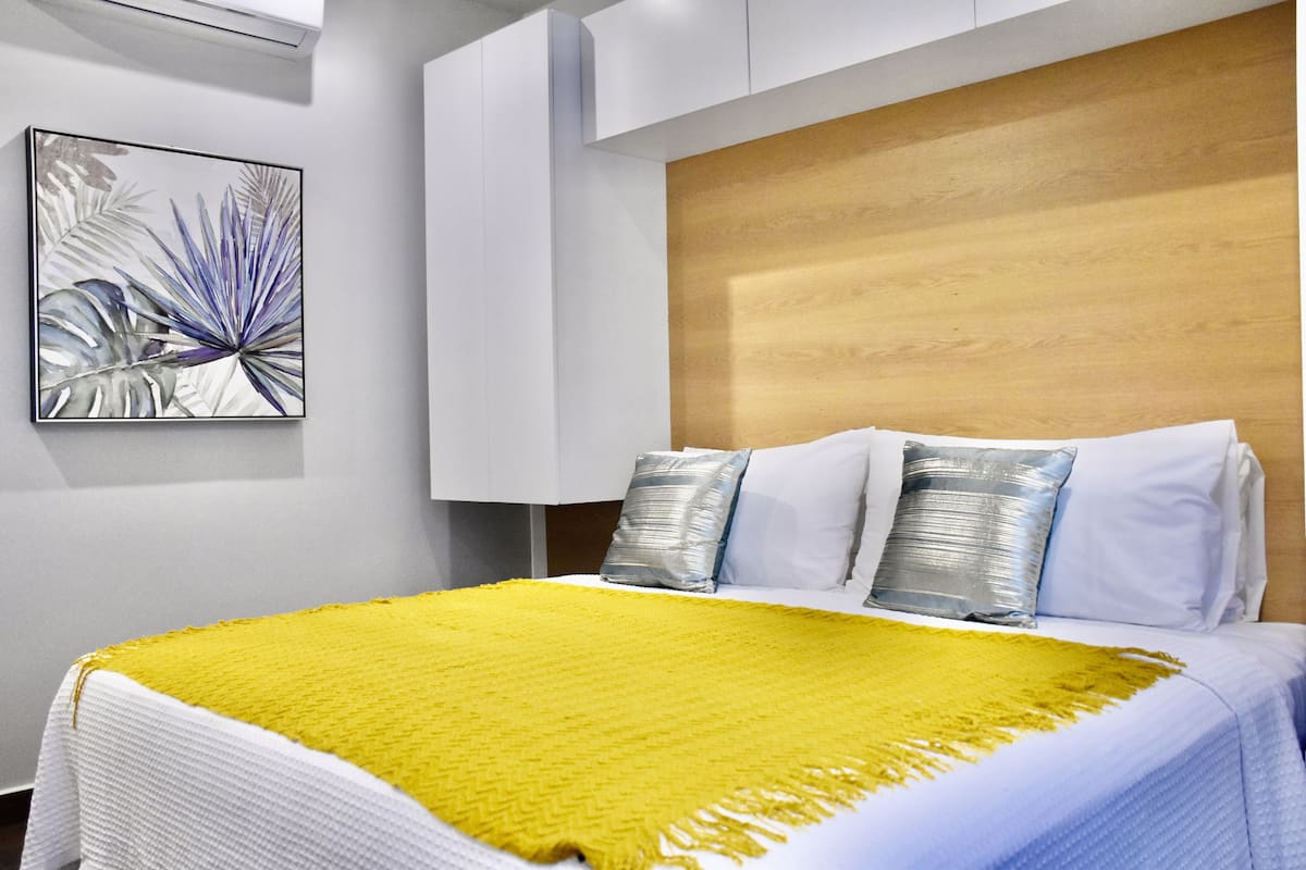 A modern bedroom with a wooden headboard, a white bedspread, and a yellow throw blanket.