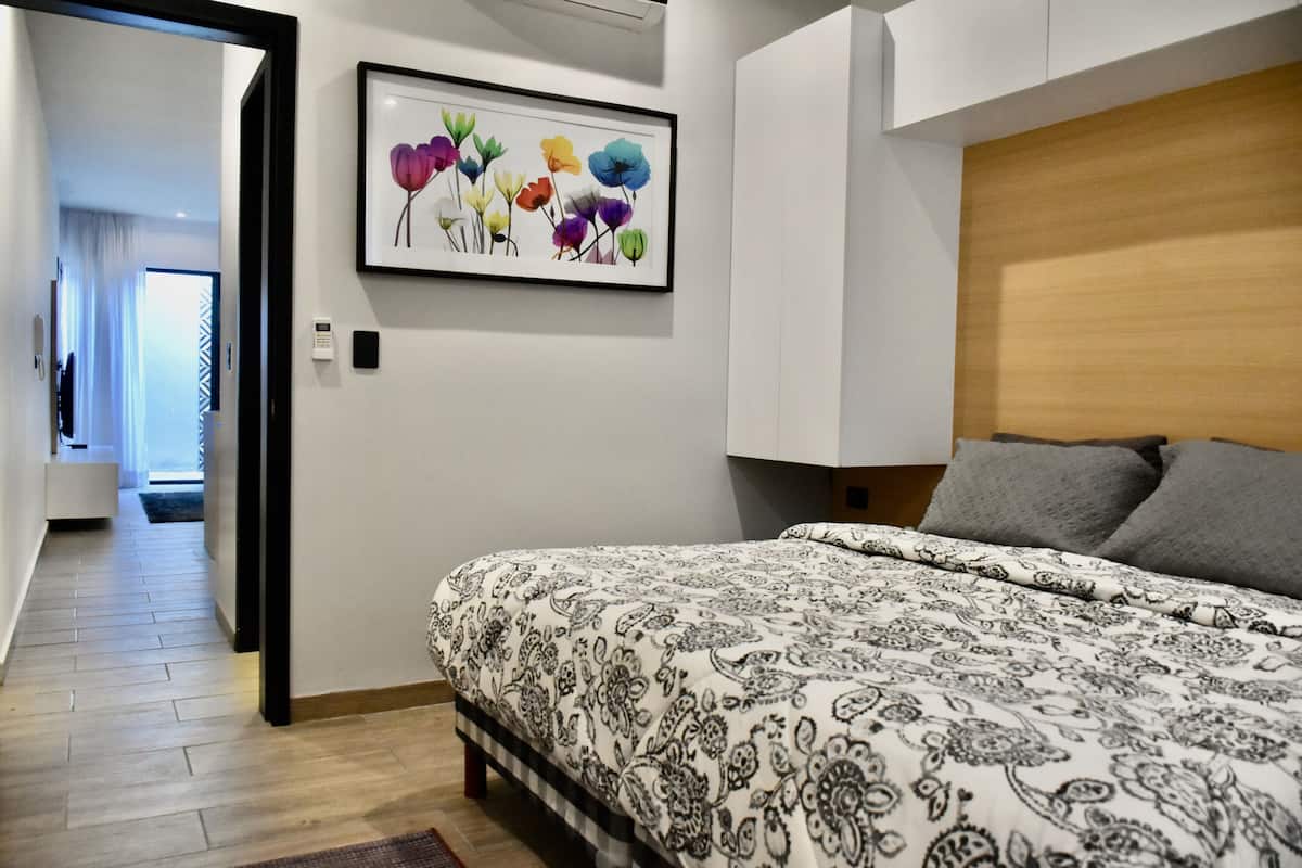 A bedroom with a bed, a wooden headboard, a framed floral artwork, and a hallway leading to another room.