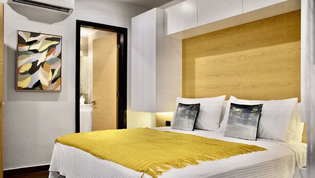 A modern hotel room with a large bed, a wooden headboard, and a yellow throw blanket. - Vedra Apartments (Playa del Carmen)