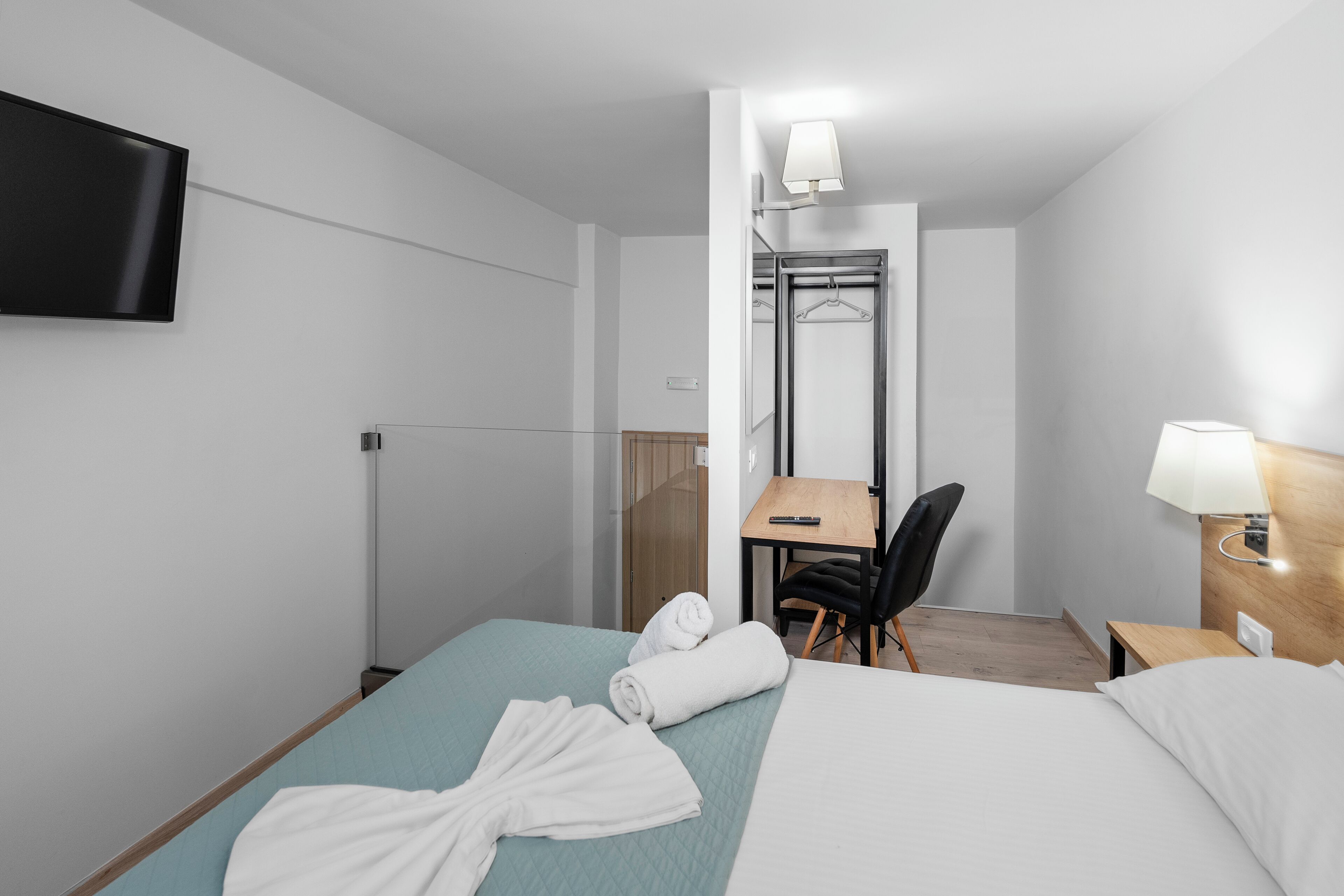 A hotel room with a bed, a desk, a chair, a TV, and a mirror.