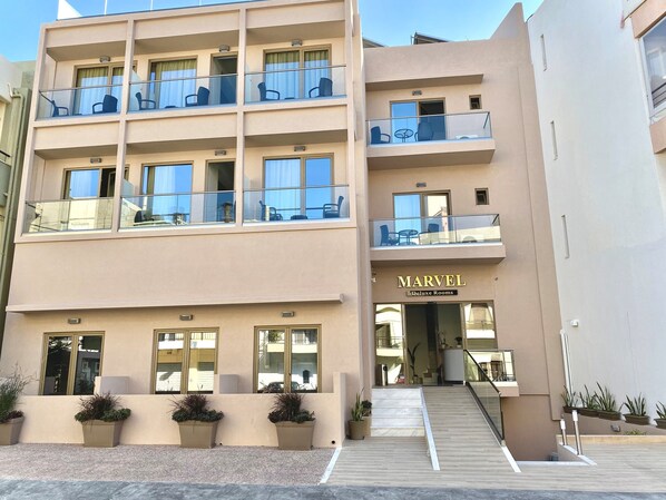 A multi-story hotel with balconies, a sign for 'Marvel Deluxe Rooms', and potted plants at the entrance. - Marvel Deluxe Rooms (Heraklion)