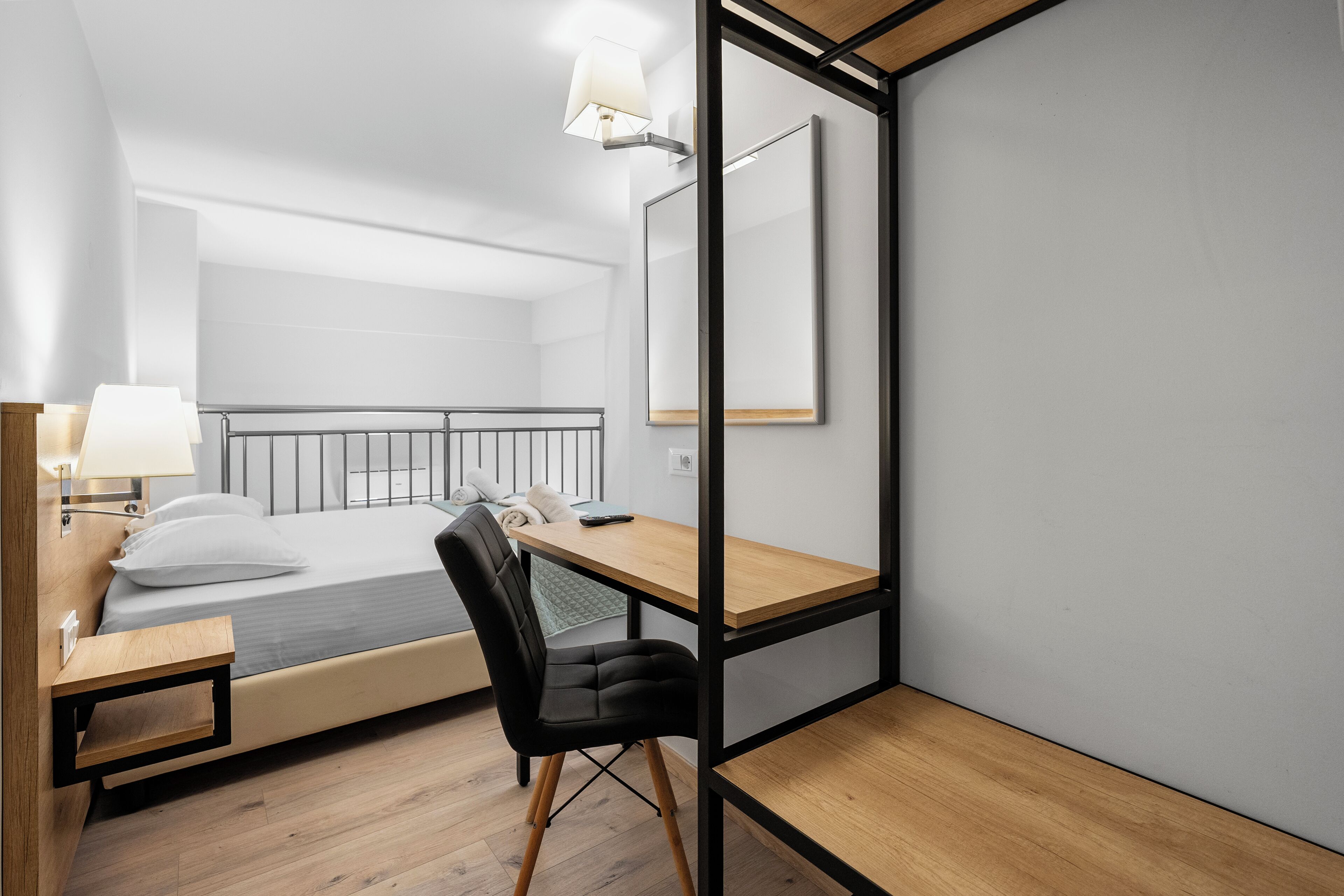 A modern hotel room with a bed, a desk, a chair, and a mirror.