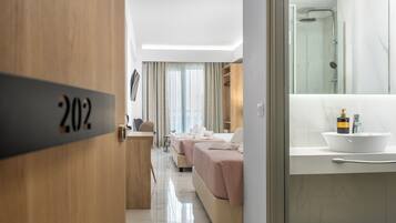 A hotel room with a wooden door labeled "202", a bed with a pink bedspread, a bedside table, a mirror, and a bathroom with a bathtub and a sink.