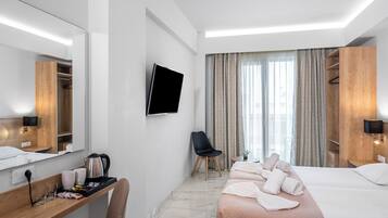 Una habitación de hotel moderna con una cama, un escritorio con hervidor, una silla, un televisor y un amplio ventanal con cortinas.