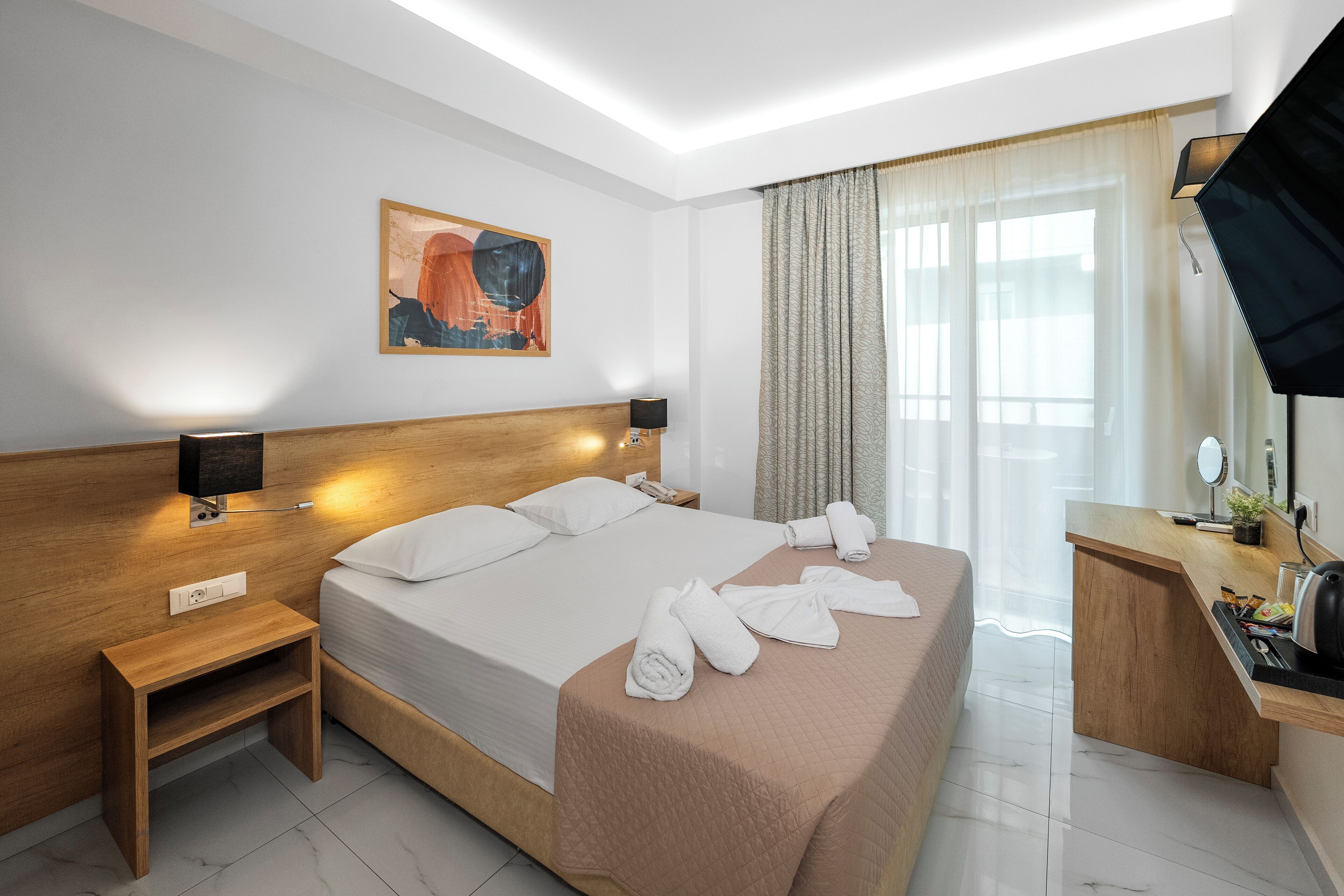A hotel room with a large bed, bedside tables, a desk with a chair, a flat-screen TV, and a window with curtains.