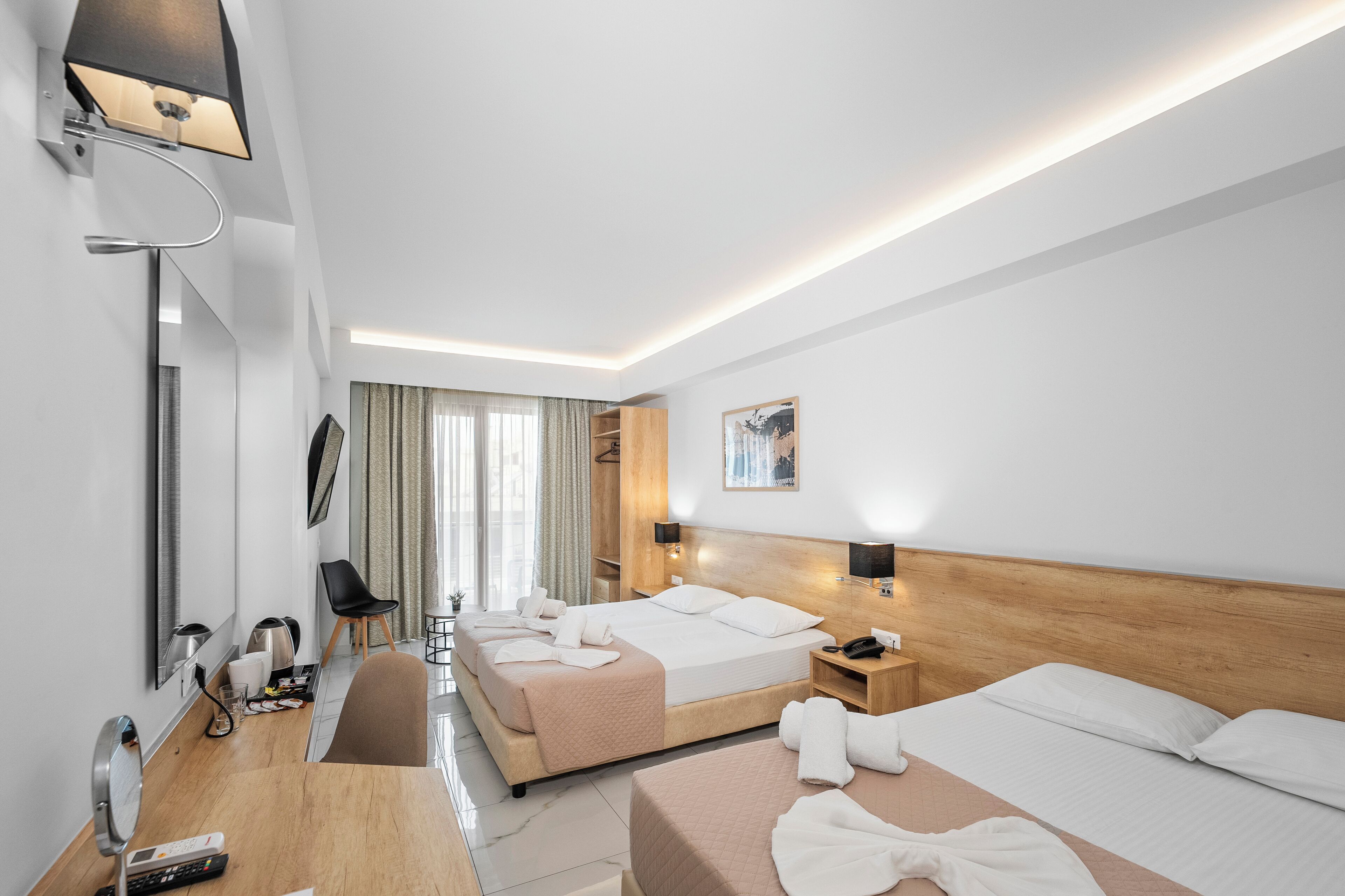 Ein Hotelzimmer mit zwei Betten, einem Schreibtisch, einem Stuhl, einem Spiegel, einer Lampe und einem Fenster mit Vorhängen.
