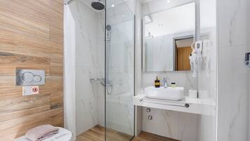 A modern bathroom with a glass shower enclosure, a white sink with toiletries, and a wooden floor.