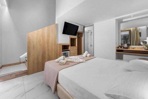 A modern hotel room with a bed, a TV mounted on a wooden panel, a shower area, and a mirror above the sink. - Marvel Deluxe Rooms (Heraklion)