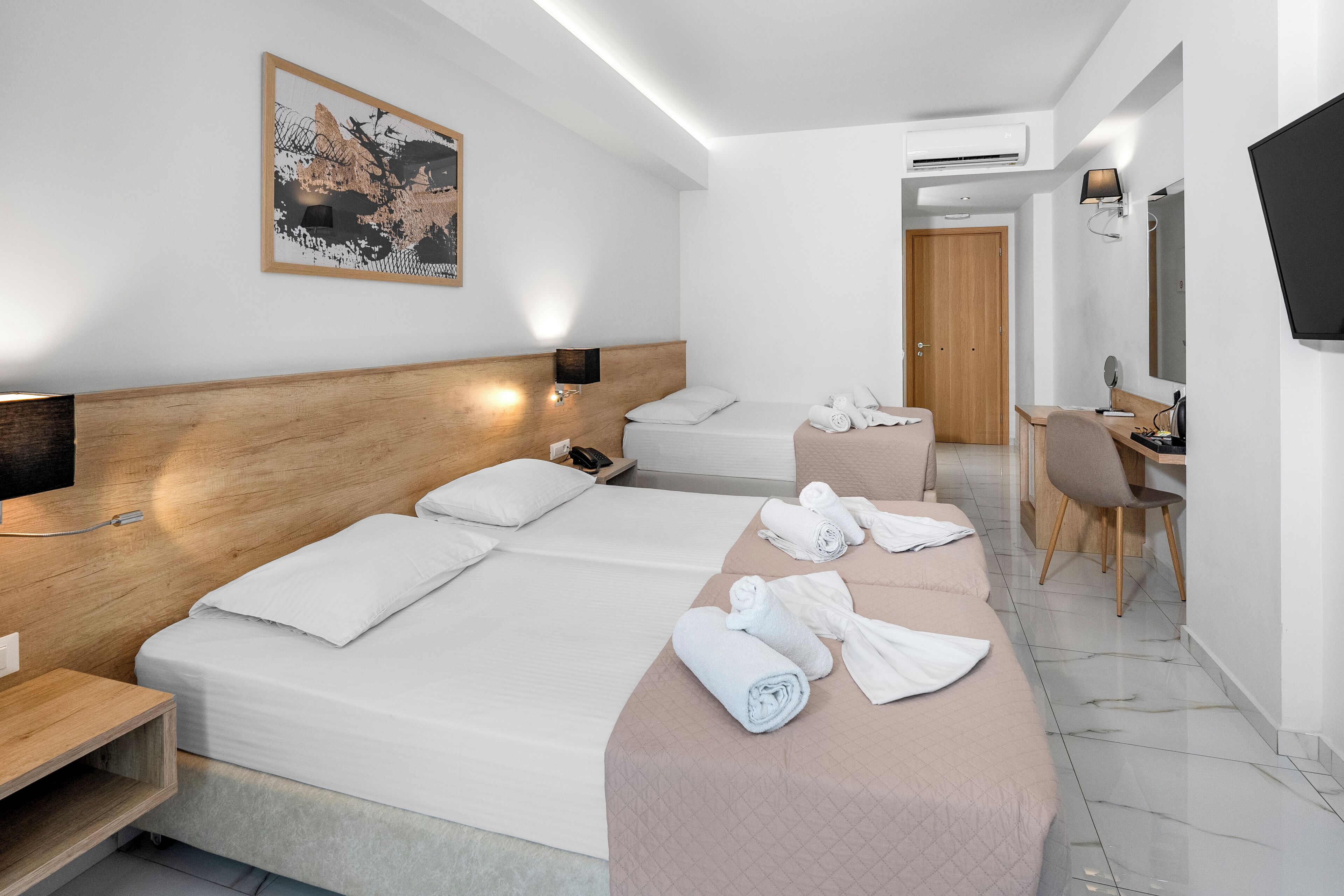 Ein Hotelzimmer mit zwei Betten, einem Schreibtisch, einem Stuhl, einem Fernseher und einer Klimaanlage.