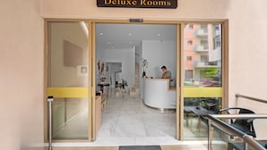 Entrada de un hotel con mostrador de recepción, puerta de cristal y vista del interior.