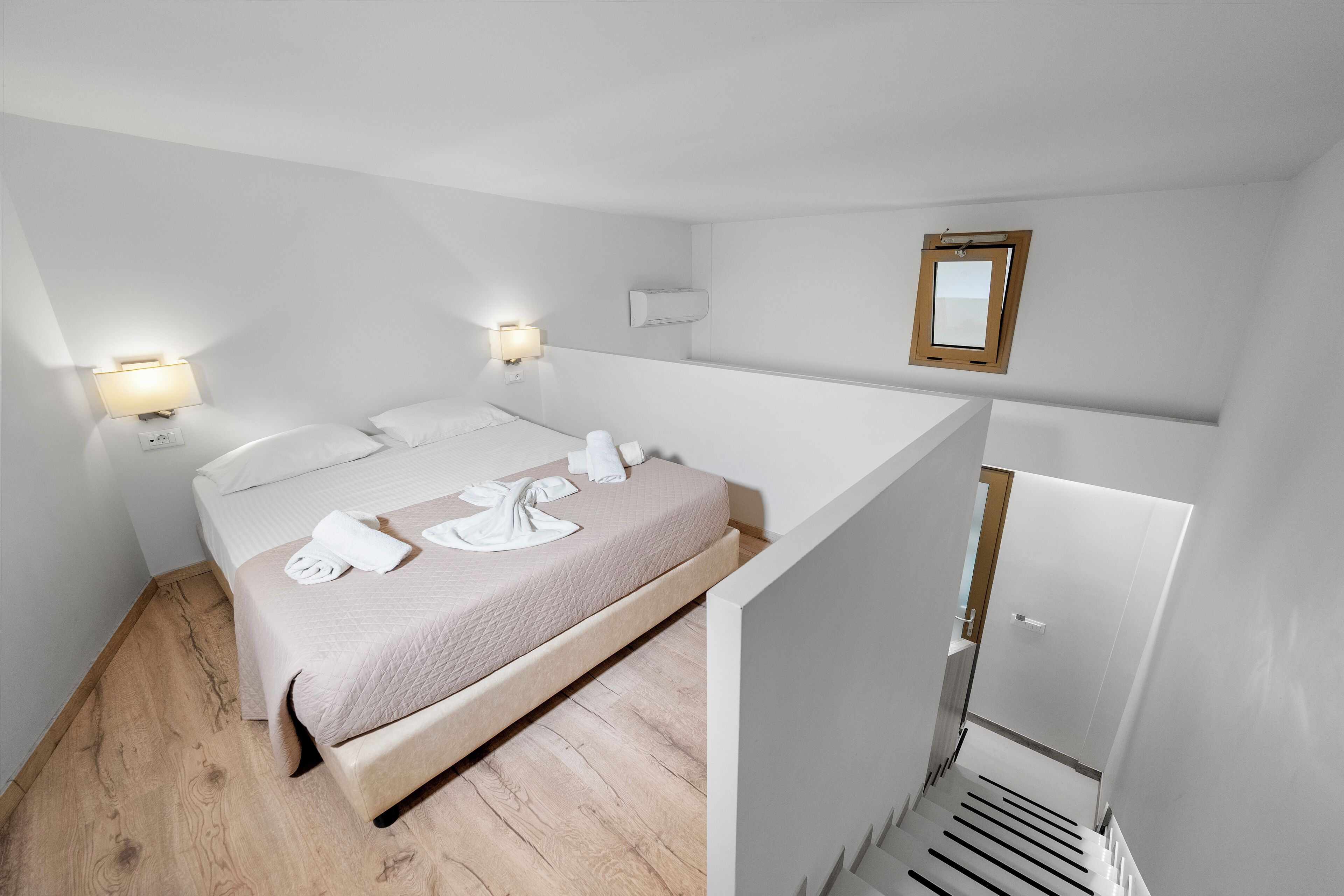 A modern hotel room with a bed, bedside lamps, a mirror, and a wooden floor.