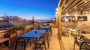 Un patio al aire libre con mesas y sillas, vistas de la ciudad y un edificio de diseño moderno.