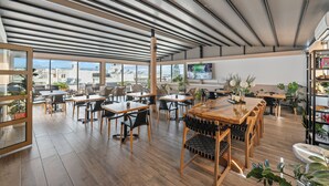 Amplio espacio interior con varias mesas y sillas, ventanas grandes que ofrecen vistas de la ciudad y un techo con vigas a la vista.