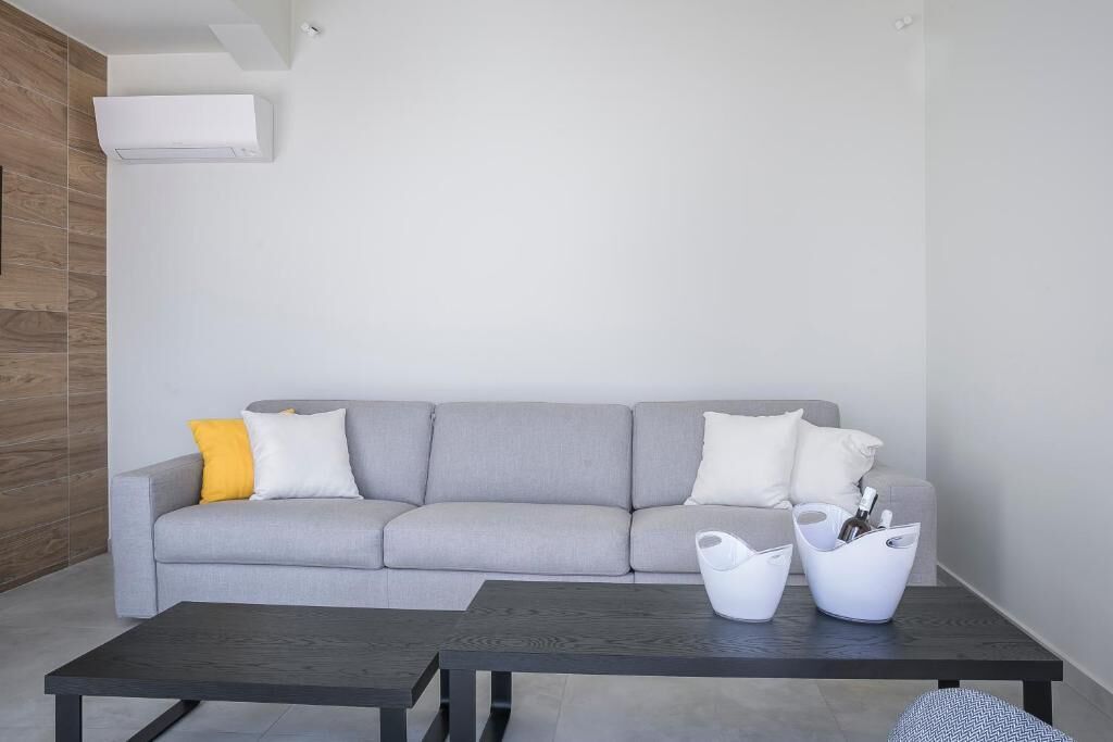 Un salon moderne avec un canapé gris, une table basse foncée et un appareil de climatisation blanc fixé au mur.