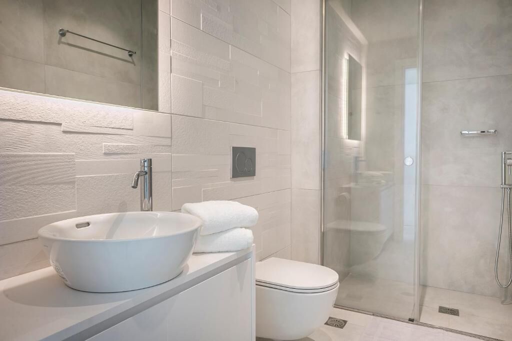 A modern bathroom with a white sink, toilet, and glass shower enclosure.