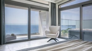 A modern bedroom with a large bed, a chair, and a balcony with a view of the sea. - Oikos Boutique Residences Private Estate (Kefalonia)