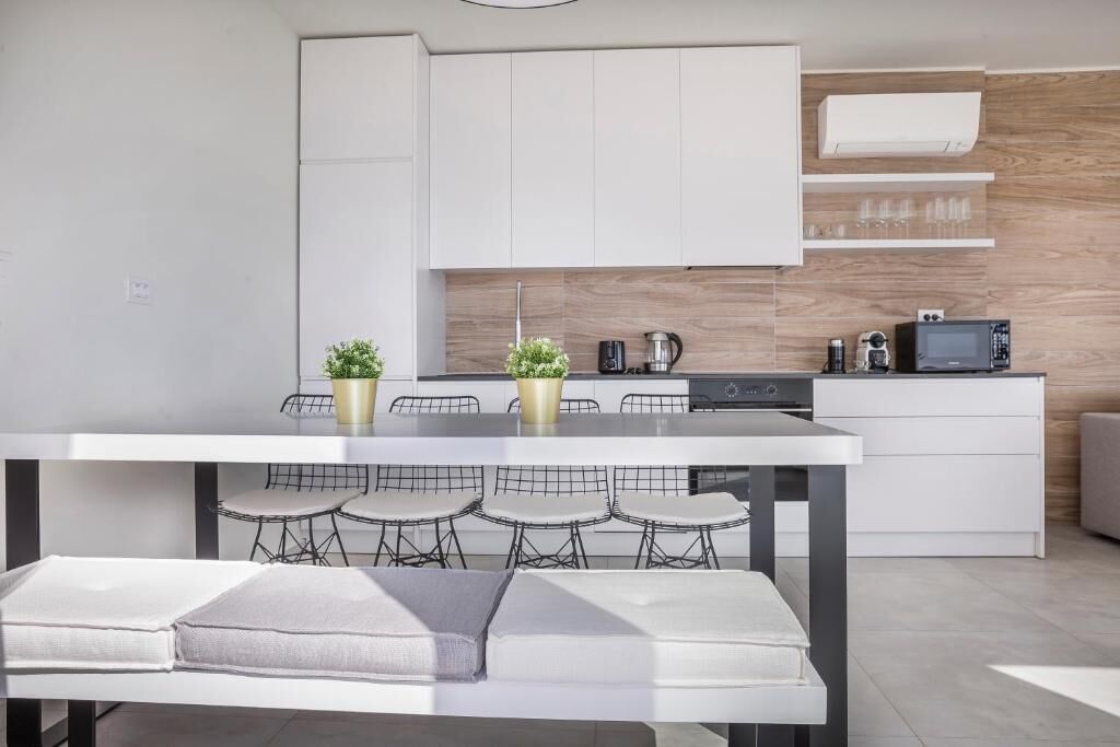 A modern kitchen with white cabinetry, a dining table with bar stools, and a built-in microwave.