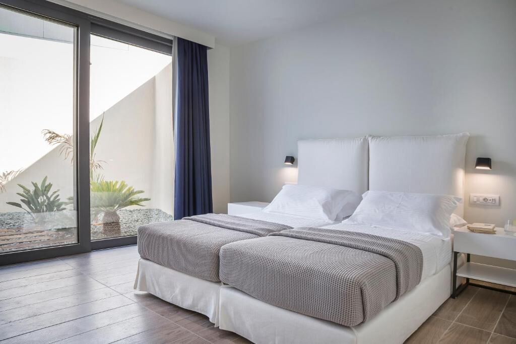 A modern bedroom with a bed, bedside tables, and a view through a large window.