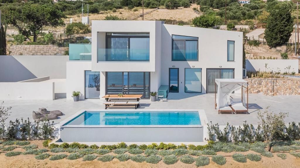 A modern two-story house with a swimming pool, outdoor seating, and a view of the surrounding landscape.