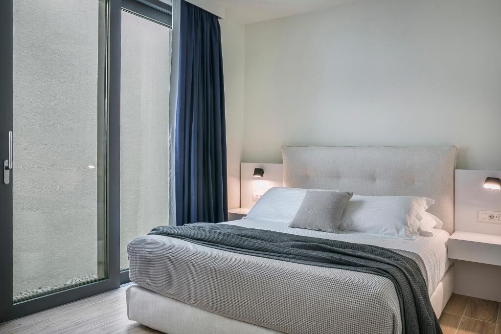 A modern hotel room with a large bed, a sliding glass door, and a nightstand with a lamp.