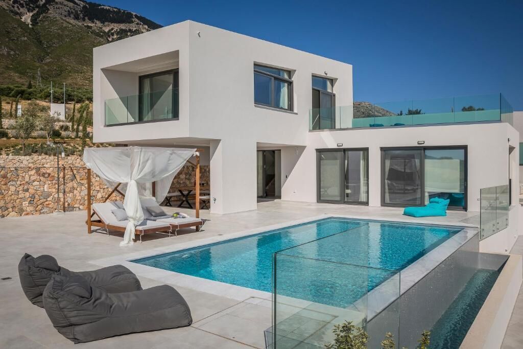 A modern two-story house with a swimming pool, outdoor seating, and a mountain backdrop.