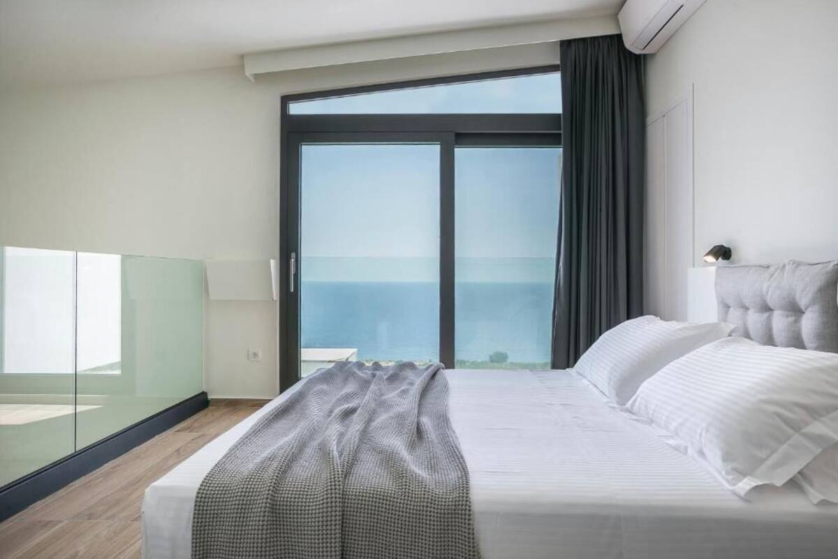 Un dormitori modern amb un llit gran, una separació de vidre i vista al mar.