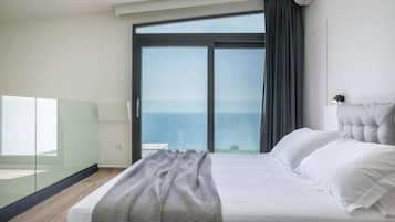 A modern bedroom with a large bed, a glass partition, and a view of the sea.