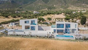 A modern two-story house with a swimming pool, surrounded by a dry landscape and mountains. - Oikos Boutique Residences Private Estate (Kefalonia)