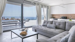 A modern living room with a grey sofa, a dining table, and a view of the ocean. - Oikos Boutique Residences Private Estate (Kefalonia)