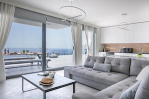 Una sala de estar moderna con un sofá gris, una mesa de comedor y vistas al océano.
