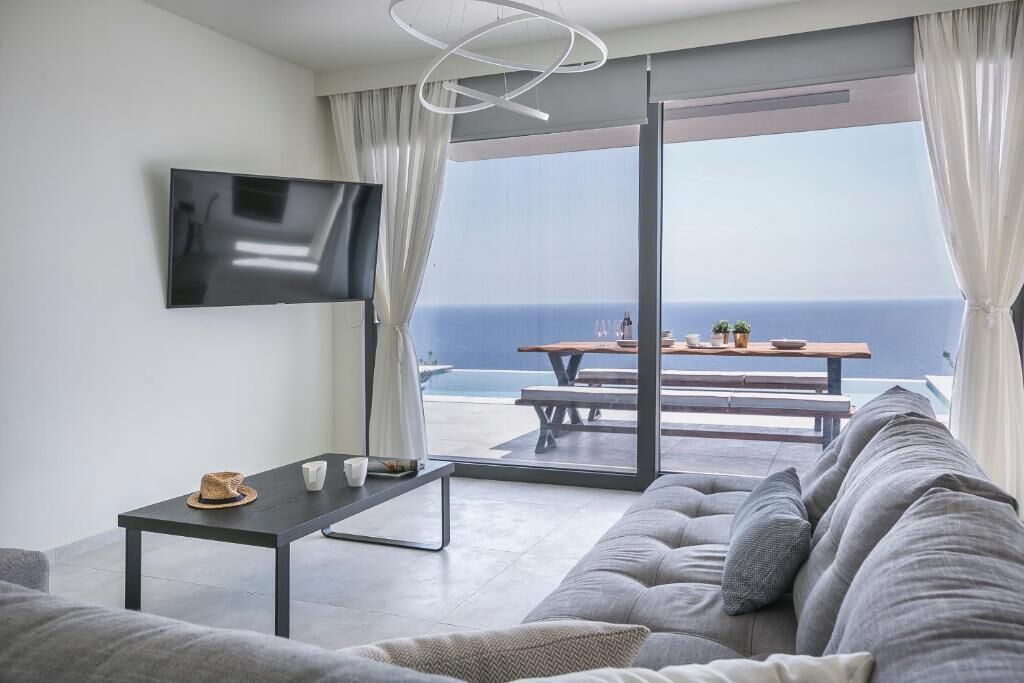 Una sala moderna con sofá, una mesa de centro y televisor. Cuenta con un balcón con mesa y sillas, y vistas al océano.
