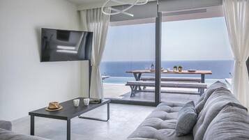 Una sala moderna con sofá, una mesa de centro y televisor. Cuenta con un balcón con mesa y sillas, y vistas al océano.