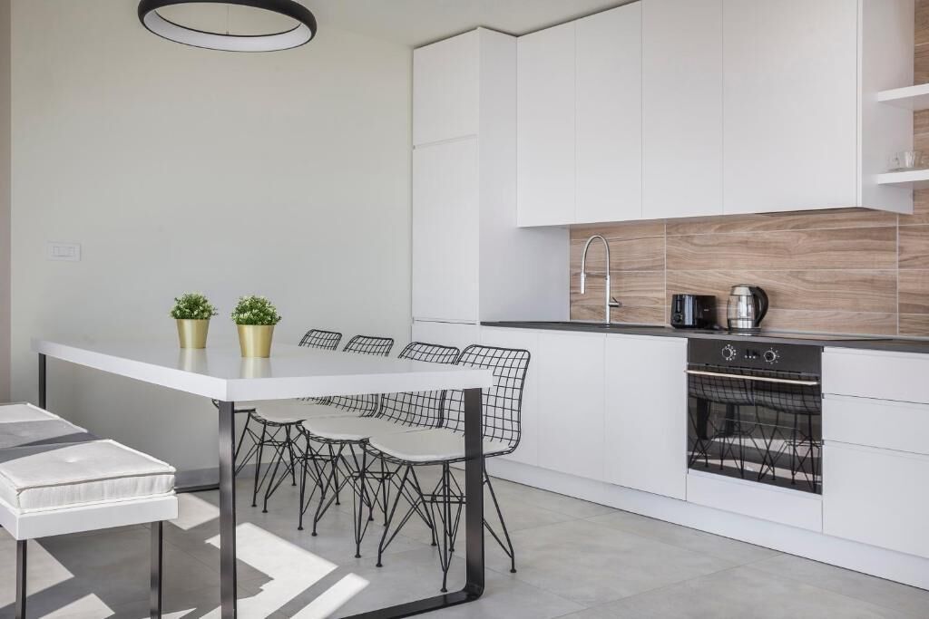 Une cuisine moderne avec des meubles blancs, une table à manger avec des chaises et un four encastré.