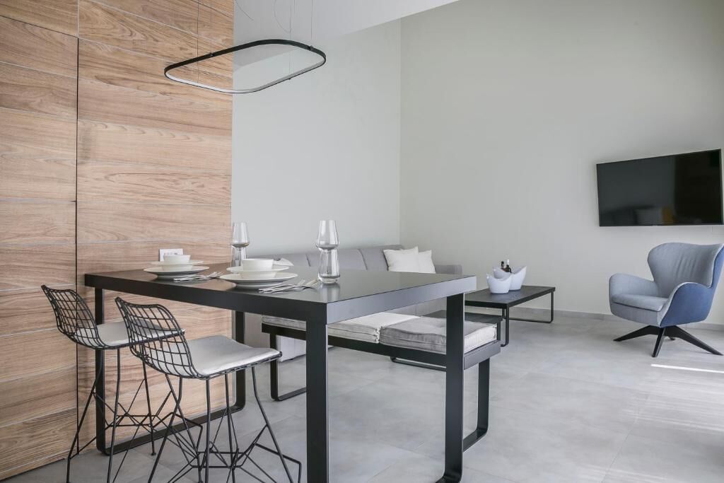 Un comedor moderno con una mesa negra, sillas blancas, un sofá y un televisor montado en la pared.