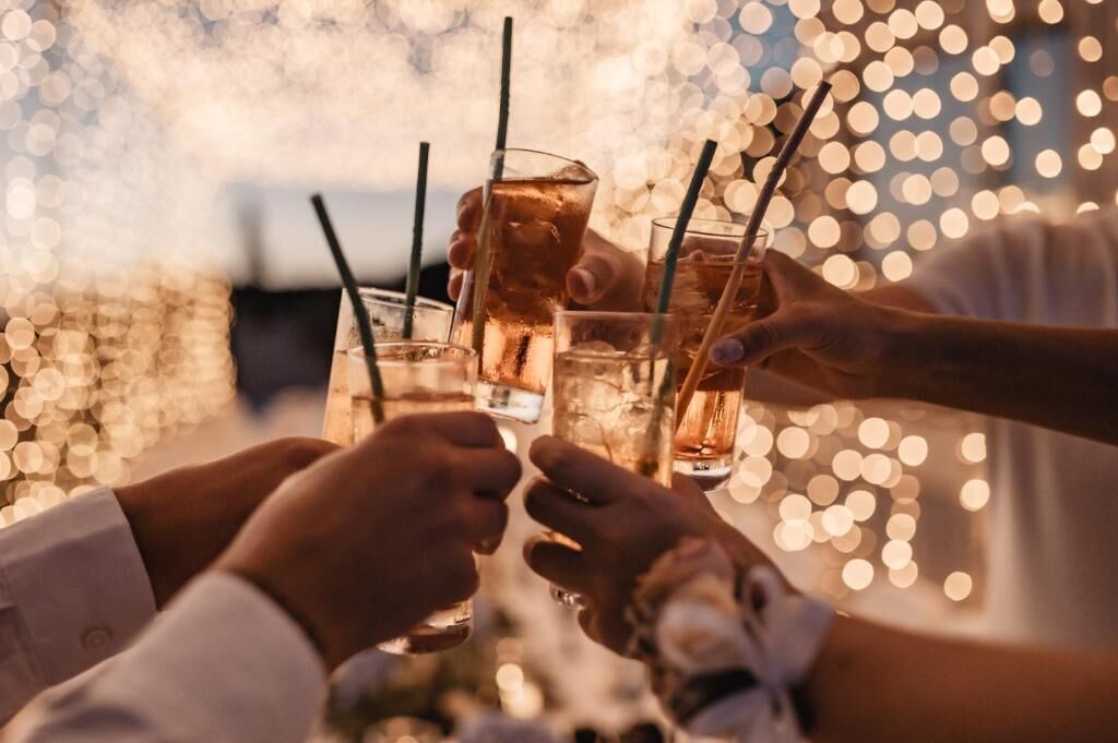 A group of people toasting with drinks at a table with a blurred background of lights.