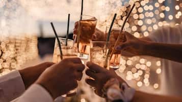 A group of people toasting with drinks at a table with a blurred background of lights.