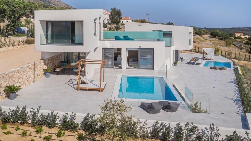 A modern two-story house with a swimming pool, outdoor seating, and a view of the surrounding landscape.