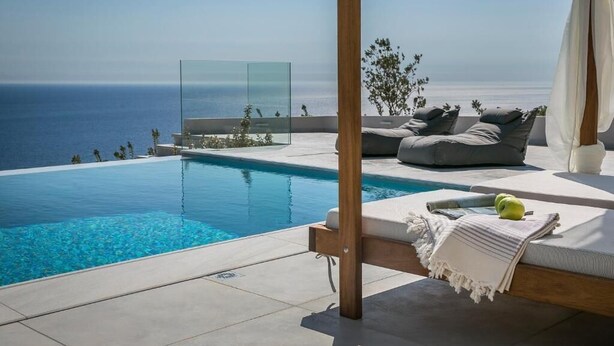 A modern infinity pool with a clear view of the ocean, a wooden pergola, and a cozy seating area with cushions and a blanket. - Oikos Boutique Residences Private Estate (Kefalonia)